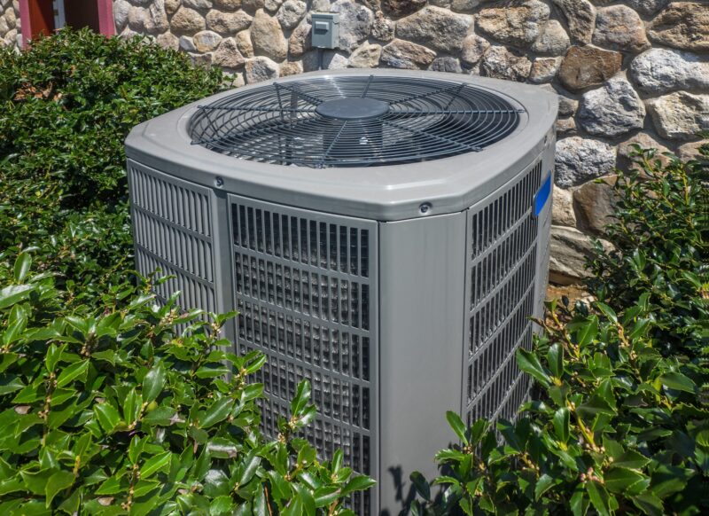 an outdoor air conditioning system surrounded by plants on the side of a home