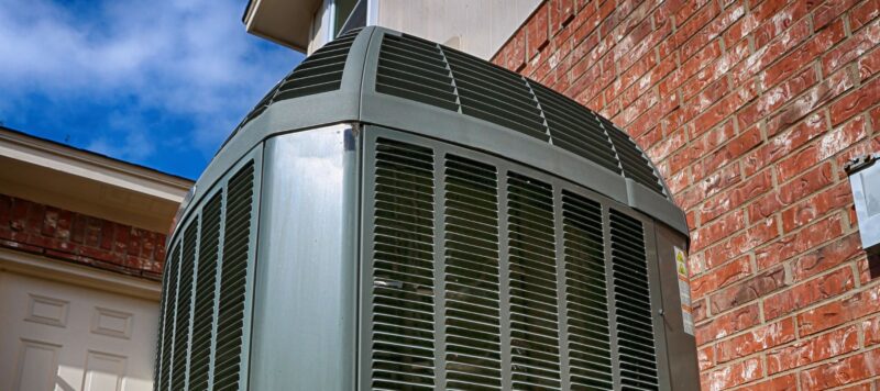 Close-up of a large outdoor air conditioning unit installed against a brick wall on a clear day